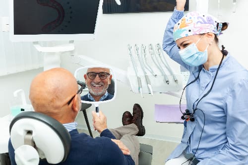 older man smiling in mirror, happy with new dental implants
